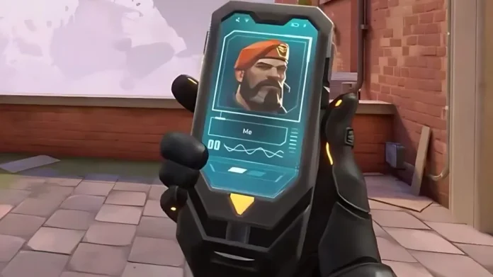 The image shows a first-person view of a player in Valorant holding a high-tech handheld device, displaying a digital card with the image of an agent, complete with vital signs and a character ID. This device exemplifies the new item in Valorant, adding strategic depth and interactivity to the gameplay, allowing players to access critical information or capabilities on the go.