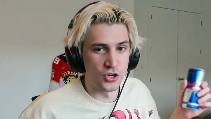 Image of popular streamer xQc, wearing headphones and speaking into a microphone while holding a can of energy drink, in a room with a gaming chair and minimalist decor.